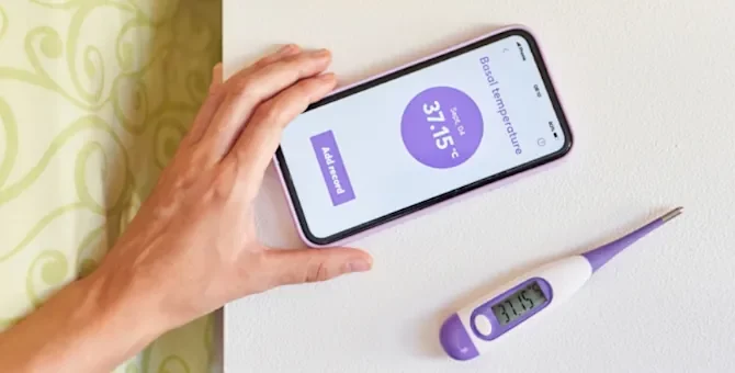 Kobieta trzyma w ręce telefon z aplikacją do pomiaru temperatury ciała