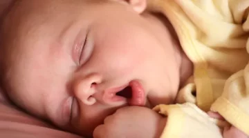 Śpiące niemowlę w żółtym stroju z otwartą buzią leży na różowej pościeli