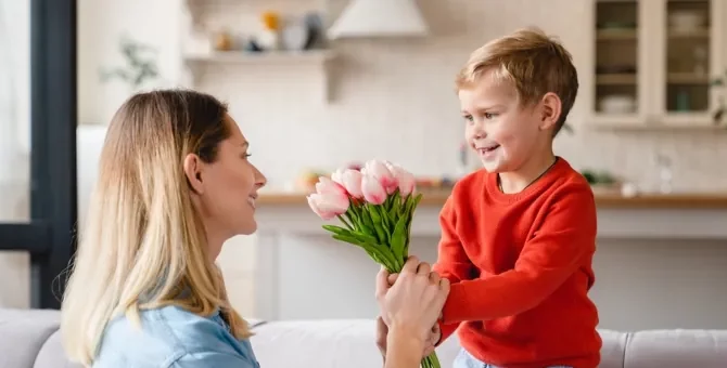 Radosny chłopiec przekazuje bukiet tulipanów uśmiechniętej mamie na Dzień Matki
