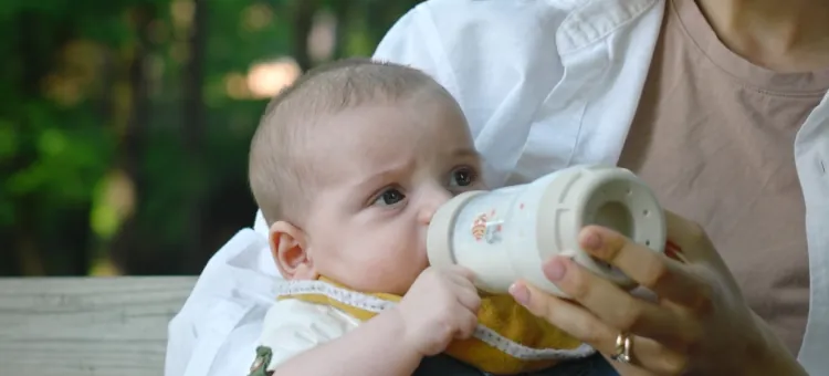 Niemowlę pije mleko podawane z butelki trzymanej przez dorosłą osobę