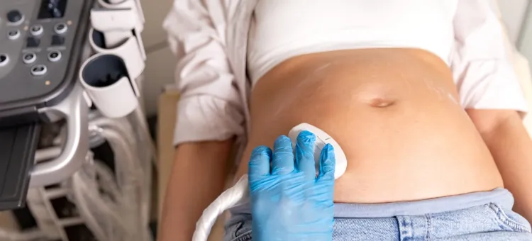 Specjalista wykonuje diagnostykę obrazową okolic brzucha kobiety ciężarnej za pomocą głowicy ultrasonografu, zbliżenie na rękę i brzuch