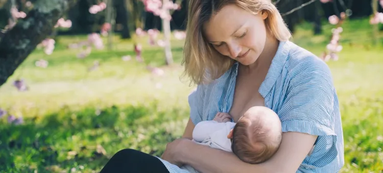 Kobieta z miłością pochyla się nad karmionym maluszkiem wśród zieleni i kwitnących drzew
