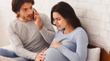 Ciąża u kobiety z bólami porodowymi, a jej partner telefonuje po ratunek, siedzą na łóżku