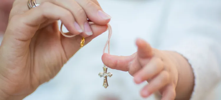 Gest opieki i dawania, gdzie dłoń dorosłego przesuwa święty przedmiot krzyżyk w kierunku dziecka