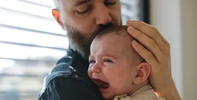 Mężczyzna delikatnie koi płaczące niemowlę z otwartą buzią