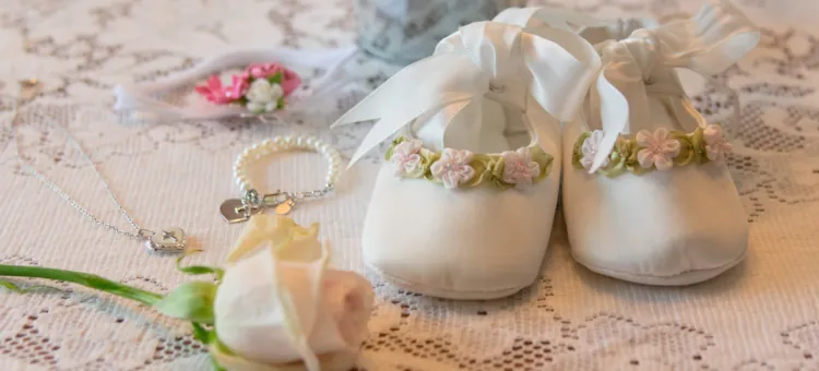 Jak personalizować wyjątkowy prezent na chrzest dziewczynki? Miękkie buciki, drobne ozdoby i róża delikatnie ułożone na serwecie