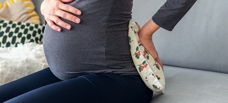 Co na ból pleców w ciąży – inne skuteczne sposoby Kobieta w ciąży przykładająca ciepły okład do dolnej części pleców