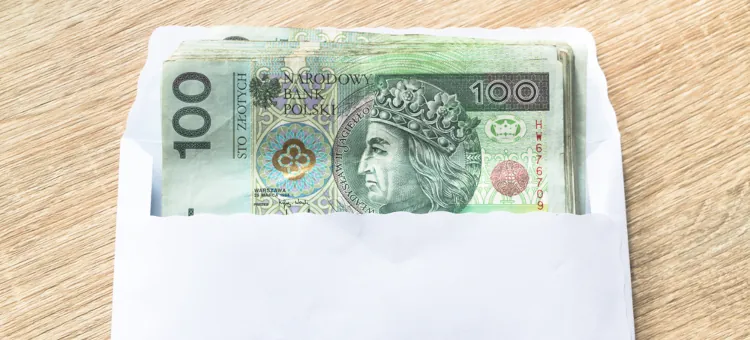Banknoty stuzłotowe włożone do białej koperty na drewnianym podłożu