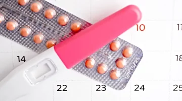 Pigułki antykoncepcyjne obok testu ciążowego na tle zaznaczonego kalendarza