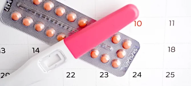 Pigułki antykoncepcyjne obok testu ciążowego na tle zaznaczonego kalendarza