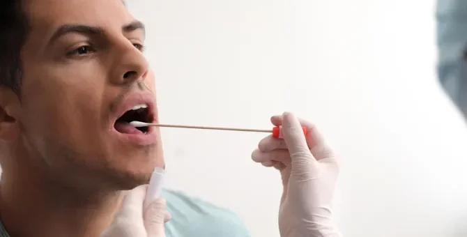 Mężczyzna przechodzący pobieranie próbki dna z jamy ustnej patyczkiem w celu np. zbadania możliwego ojcostwa