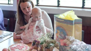 Opiekuńcza mama trzyma swoją córeczkę podczas wesołego przyjęcia chrzcielnego, pełnego słodkości i upominków