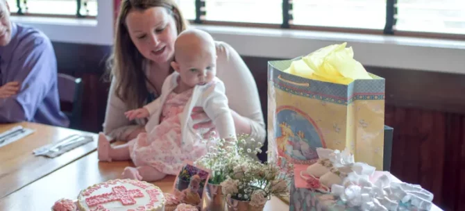 Opiekuńcza mama trzyma swoją córeczkę podczas wesołego przyjęcia chrzcielnego, pełnego słodkości i upominków