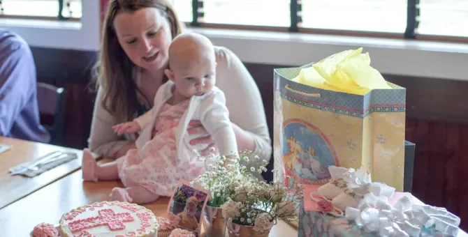 Opiekuńcza mama trzyma swoją córeczkę podczas wesołego przyjęcia chrzcielnego, pełnego słodkości i upominków