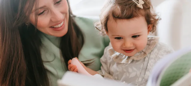Szczęśliwa mama ogląda książkę ze swoim maluchem, który trzyma różowy przedmiot w rączce