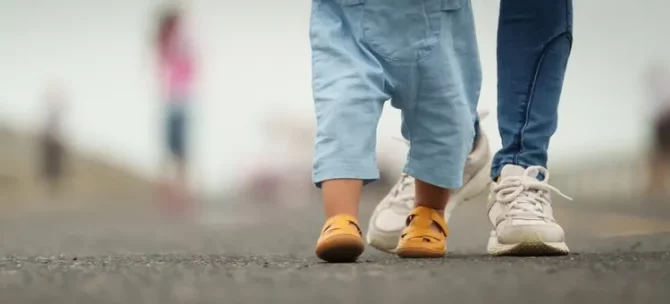 Drobne nóżki dziecka w sandałach towarzyszą dorosłym stopom na spacerze