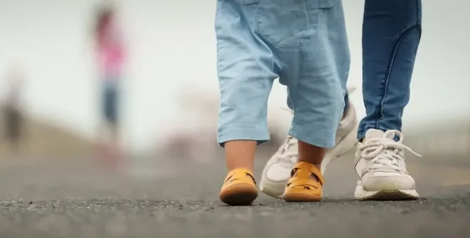 Drobne nóżki dziecka w sandałach towarzyszą dorosłym stopom na spacerze