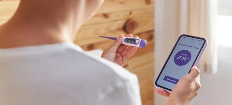 Osoba monitorująca temperaturę ciała za pomocą cyfrowego termometru i aplikacji mobilnej