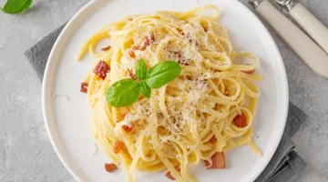 Makaron carbonara z chrupiącym boczkiem i świeżą bazylią, obficie posypany parmezanem