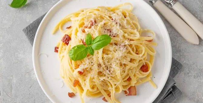 Makaron carbonara z chrupiącym boczkiem i świeżą bazylią, obficie posypany parmezanem