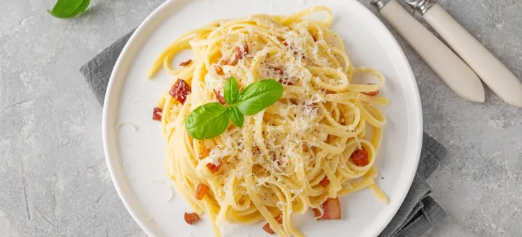 Makaron carbonara z chrupiącym boczkiem i świeżą bazylią, obficie posypany parmezanem