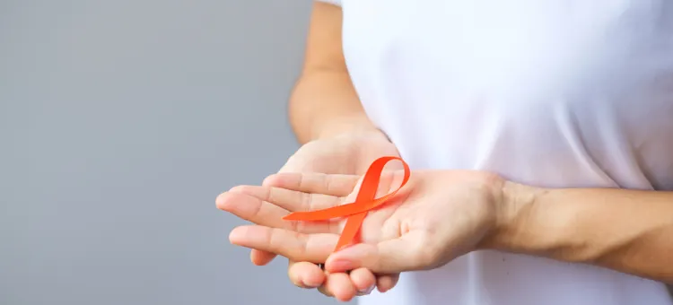 Osoba prezentująca pomarańczową kokardkę, symbolizującą walkę z białaczką, zbliżenie na ręce