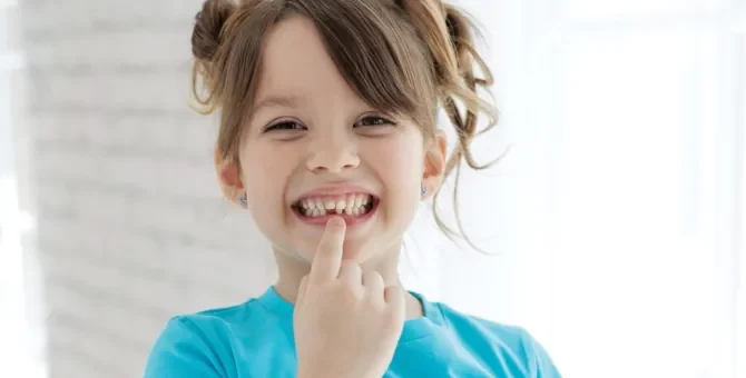 Szczęśliwe dziecko w niebieskiej koszulce prezentuje ubytek w swoim uzębieniu