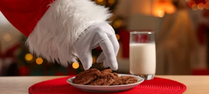 Ręka Mikołaja w białej rękawicy zmierza w kierunku kruchych przysmaków i mleka