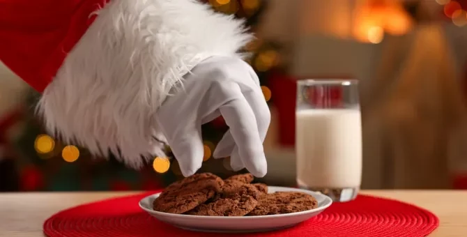 Ręka Mikołaja w białej rękawicy zmierza w kierunku kruchych przysmaków i mleka