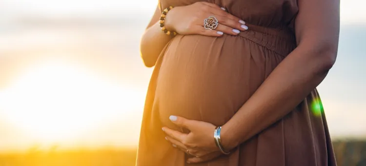Czy można pić kofeinę w ciąży? Czułe objęcie dłońmi kobiecego brzucha na tle zachodzącego słońca