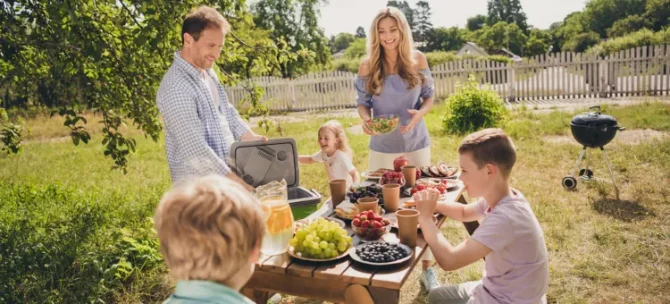 Uśmiechnięci członkowie dużej rodziny cieszą się posiłkiem na świeżym powietrzu w słoneczny dzień