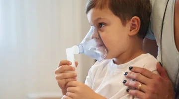 Dziecko otrzymuje wsparcie podczas terapii oddechowej w celu zmniejszenia kaszlu, ręka matki trzyma go za ramię