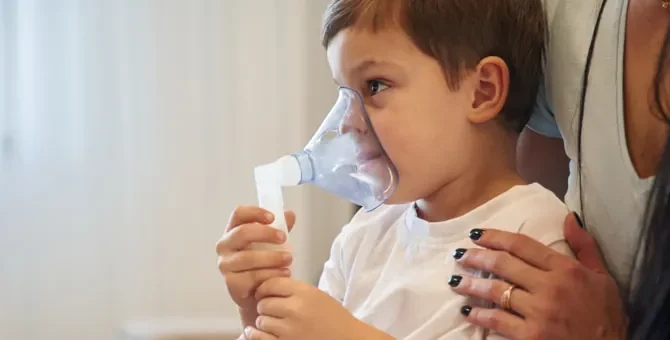 Dziecko otrzymuje wsparcie podczas terapii oddechowej w celu zmniejszenia kaszlu, ręka matki trzyma go za ramię