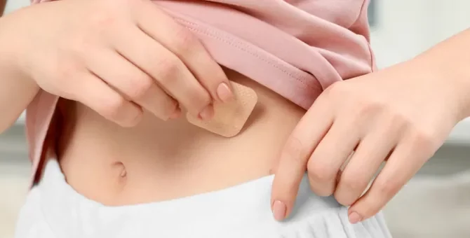 Kobieta delikatnie nakładająca niewielki antykoncepcyjny przylepiec na skórę swojego brzucha