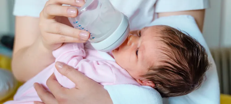 Noworodek spokojnie spożywający pokarm z butelki podtrzymywanej przez rodzica