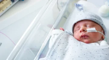 Noworodek spokojnie śpi w łóżeczku intensywnej terapii otrzymując odżywianie przez sondę