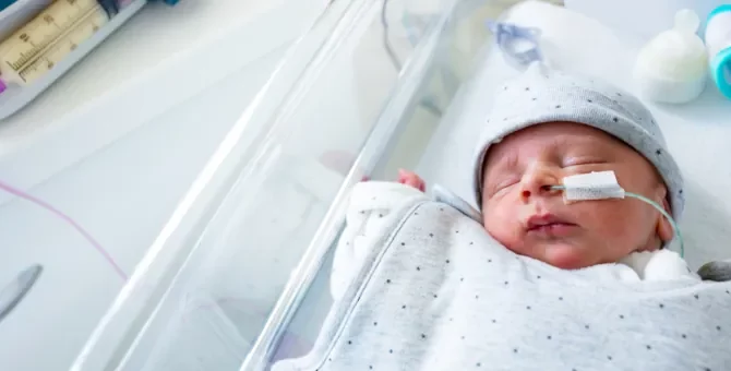 Noworodek spokojnie śpi w łóżeczku intensywnej terapii otrzymując odżywianie przez sondę