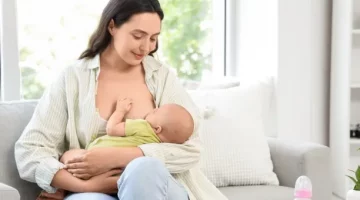 Czuła matka karmi swoje niemowlę piersią, siedząc na kanapie