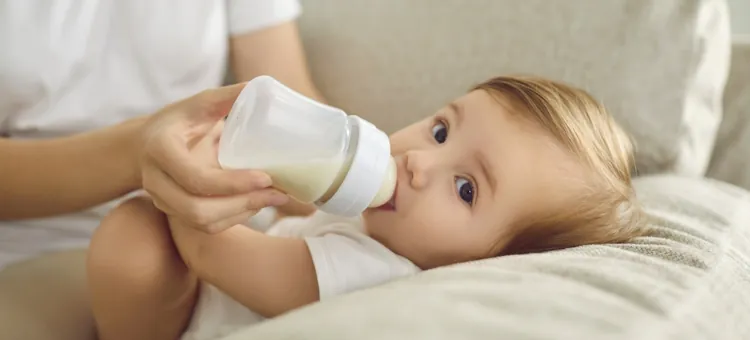 Niemowlę pijące mleko z butelki trzymanej przez dłoń dorosłego