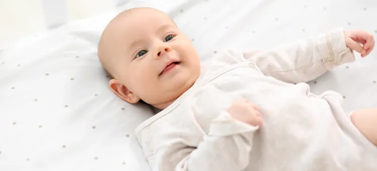 Szczęśliwy niemowlak leżący w białej pościeli, spoglądający ufnie w stronę obserwatora