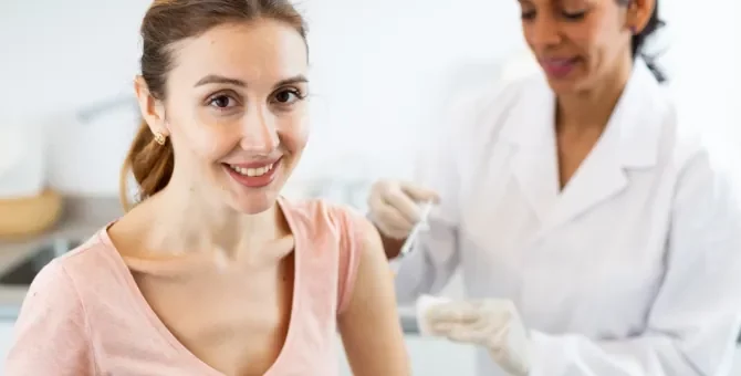 Młoda pacjentka z promiennym uśmiechem otrzymuje zastrzyk antykoncepcyjny od medyka