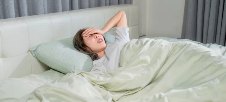 Młoda kobieta z gorączką leży w pościeli, dotykając czoła