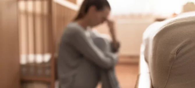 Młoda osoba z wyraźnym zmartwieniem siedzi w pomieszczeniu dla dziecka trzymając głowę w dłoniach