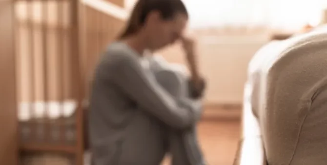 Młoda osoba z wyraźnym zmartwieniem siedzi w pomieszczeniu dla dziecka trzymając głowę w dłoniach