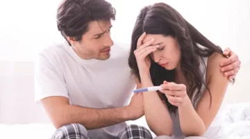 Zestresowana partnerka trzymająca domowy test ciążowy, pocieszana przez zatroskanego mężczyznę