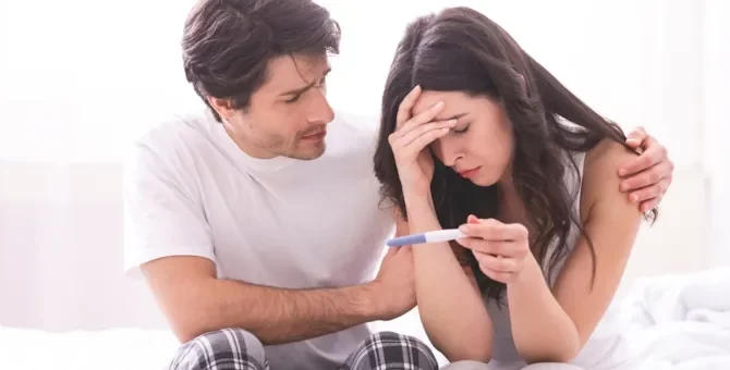 Zestresowana partnerka trzymająca domowy test ciążowy, pocieszana przez zatroskanego mężczyznę