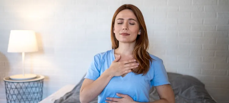Kobieta w błękitnym t-shircie wykonuje ćwiczenia oddechowe z oczami zamkniętymi i rękami na tułowiu