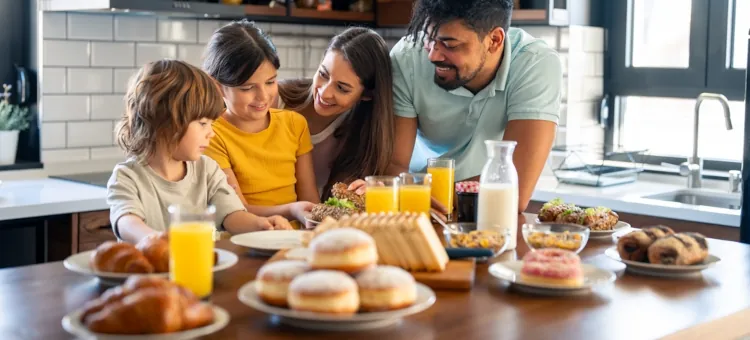 Szczęśliwi domownicy spożywający razem posiłek złożony z pączków i innych ciastek w kuchni