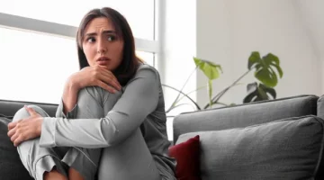 Młoda kobieta czuje lęk, skulona na sofie, jej wzrok pełen obawy