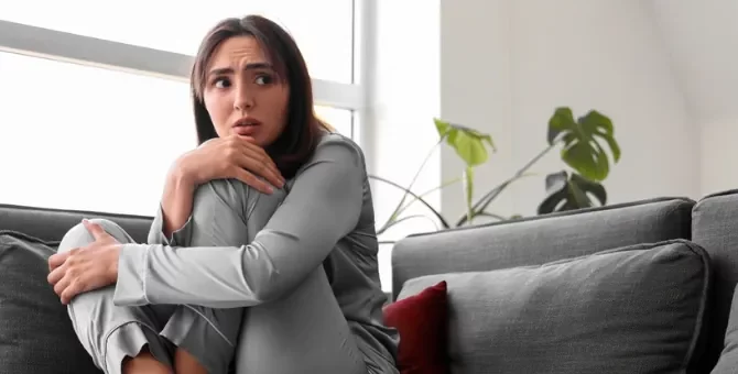 Młoda kobieta czuje lęk, skulona na sofie, jej wzrok pełen obawy